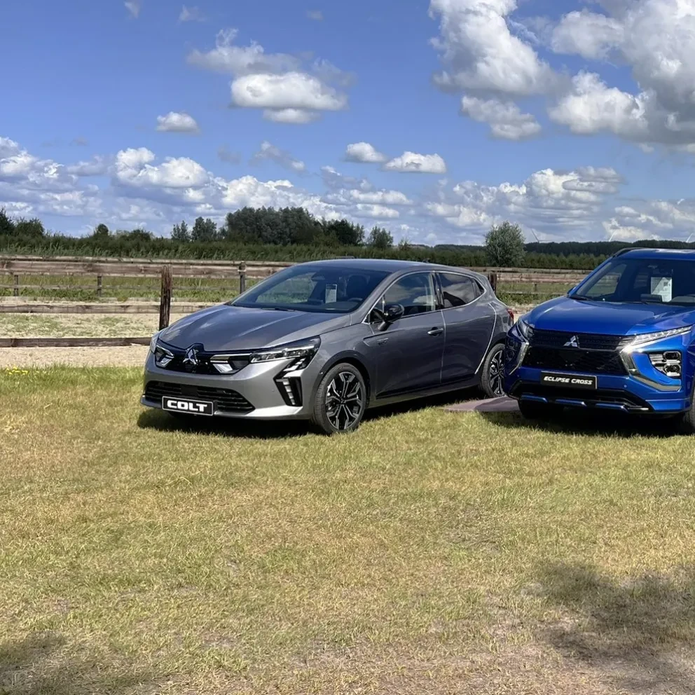 Mitsubishi Colt Volcanic Grey Mitsubishi Eclipse Cross PHEV Lightning Blue en Peugeot Partner grijs metallic op grasveld met hollandse wolkenlucht